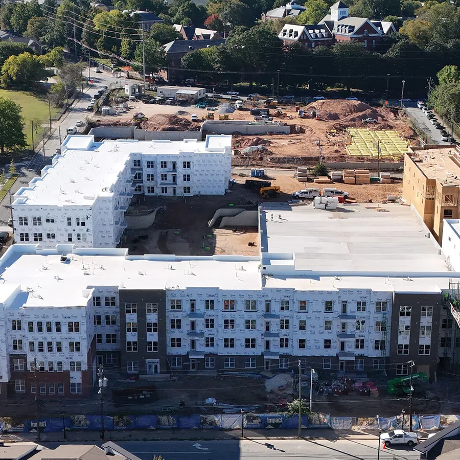 Aerial view of a large multi-story building under construction surrounded by trees and roads in a suburban area