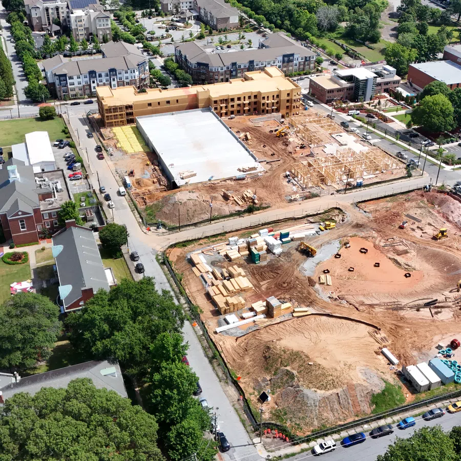Aerial view of an urban construction site with partially built structures surrounded by residential buildings and trees