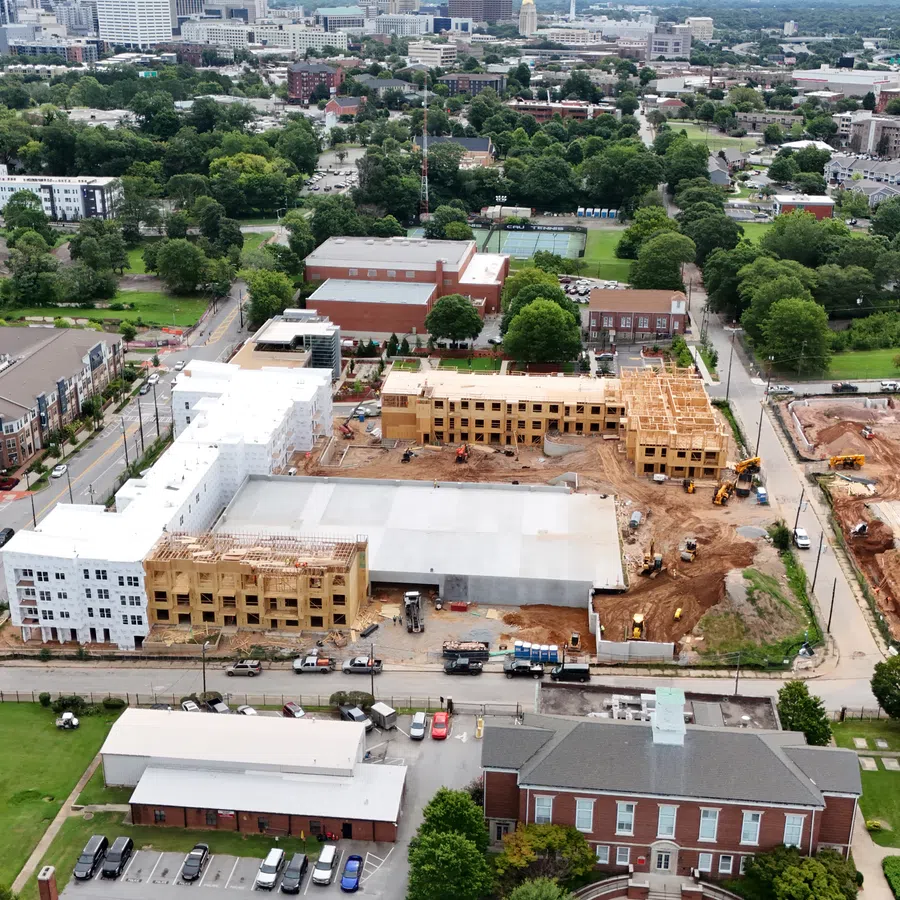 Aerial view of a mixed-use construction site with residential buildings, green spaces, and city skyline in the background.