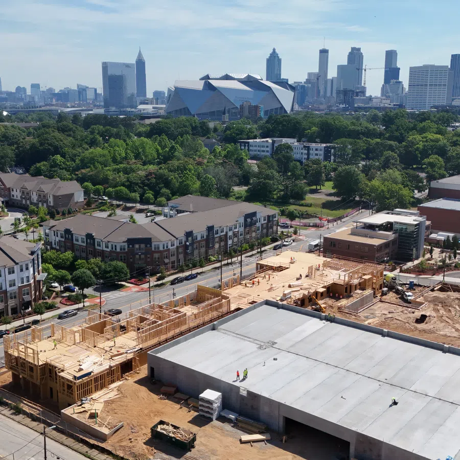 Aerial view of urban construction site with residential buildings and city skyline in the background under clear sky.
