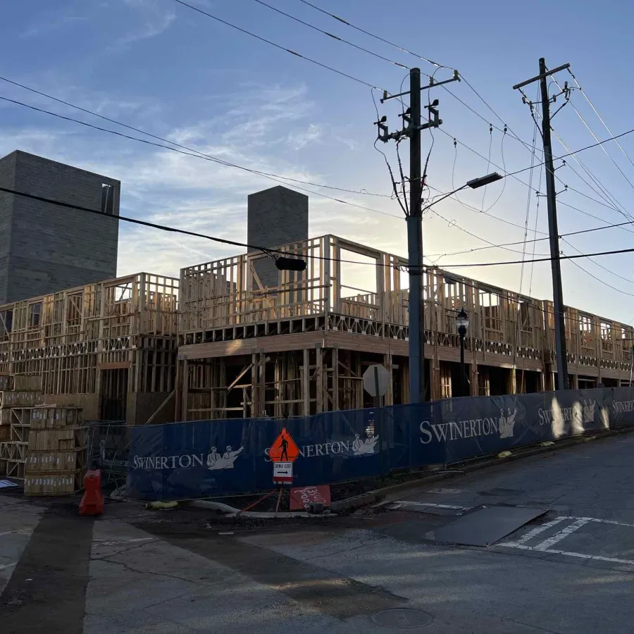 Wooden framework of a building under construction with cranes and power lines at dusk