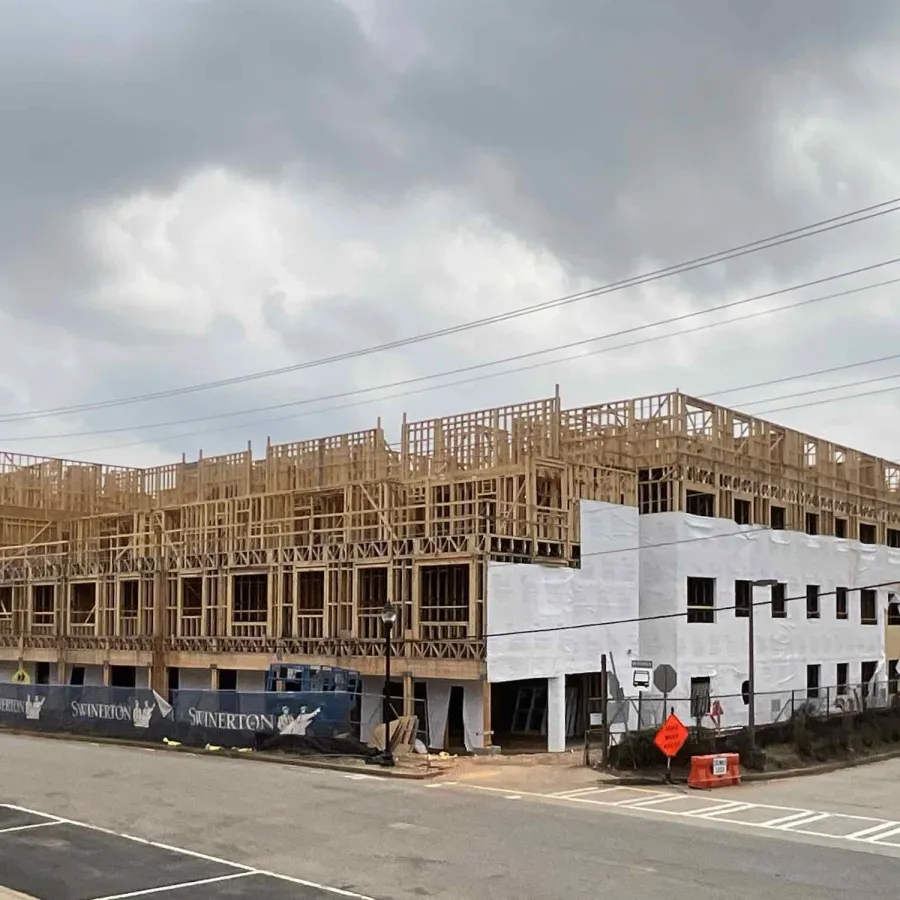 Large multi-story building under construction with wooden framing and partial white sheathing under cloudy sky.