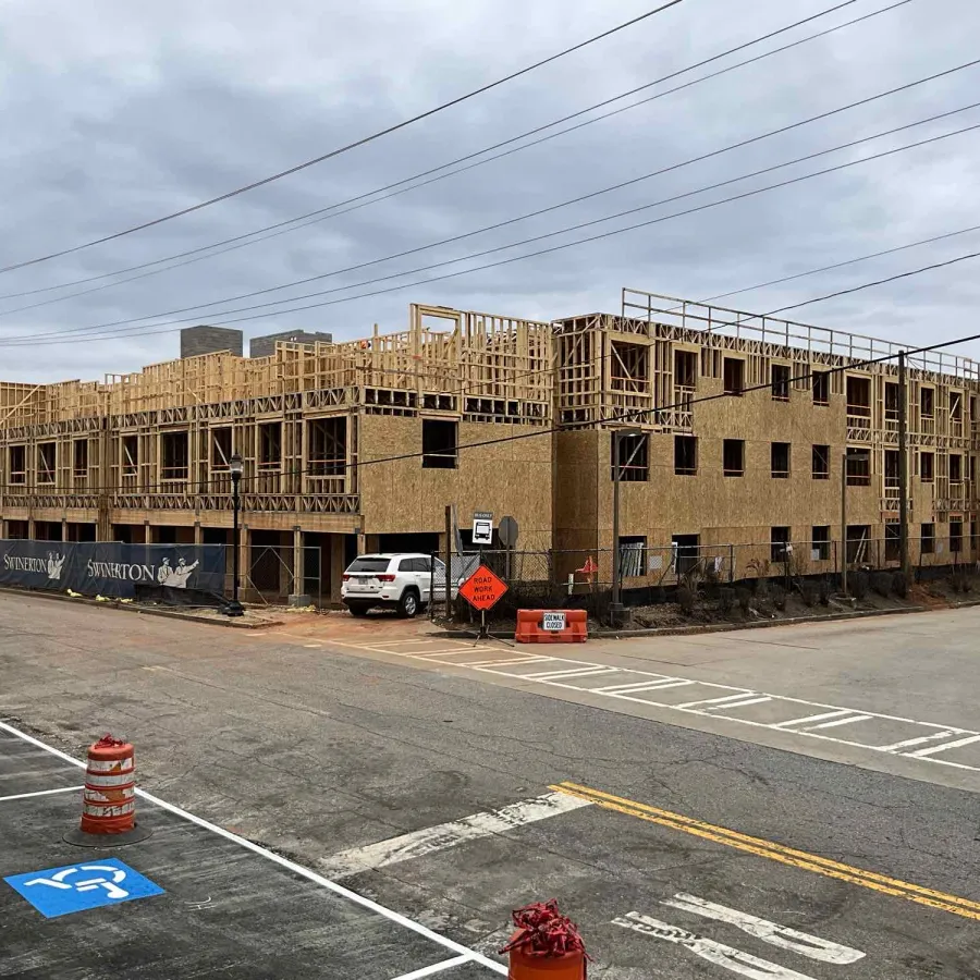 Large multi-story wooden framed building under construction near street with traffic cones and a parked white vehicle.