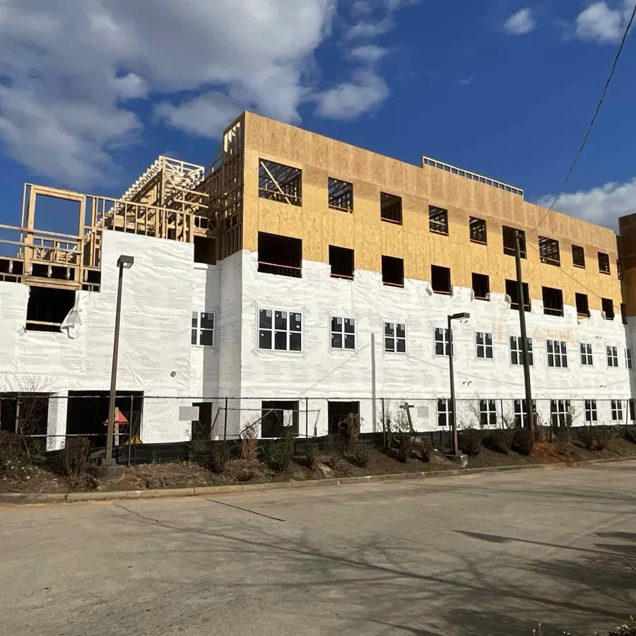 Multi-story building under construction with wooden framing and white sheathing under a partly cloudy sky.