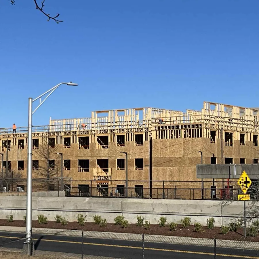Wood-framed multi-story building under construction against clear blue sky on a sunny day.