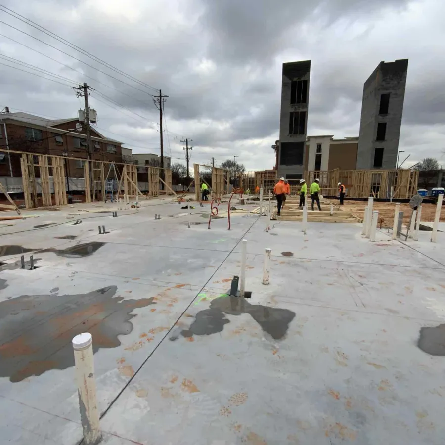 Construction site with workers assembling wooden frames on a concrete foundation under cloudy sky
