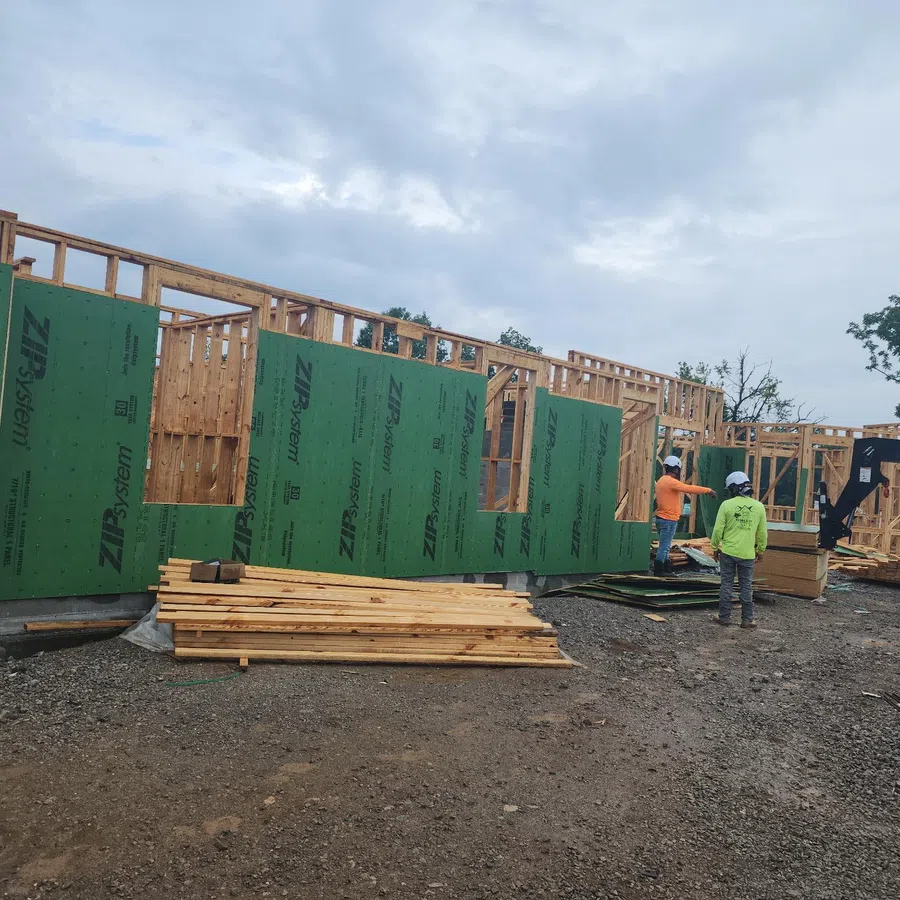 Construction site with wooden framing and green ZIP System sheathing panels being installed by workers.