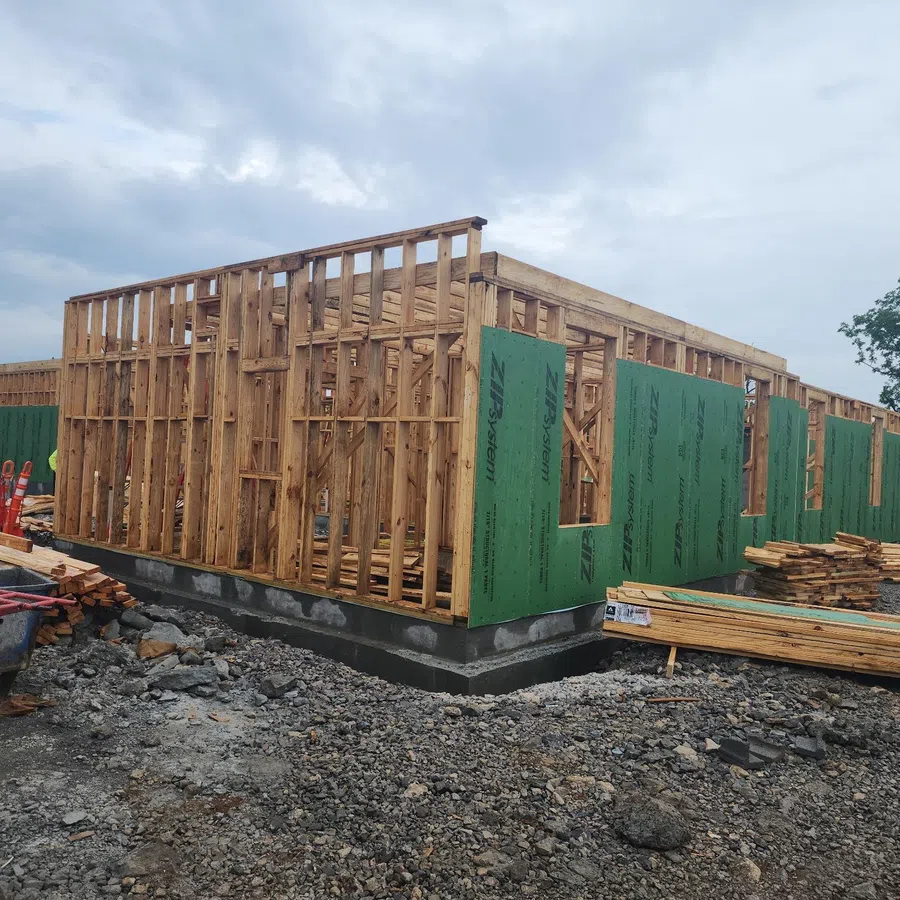 Wood framed house under construction with green sheathing and workers on a cloudy day.