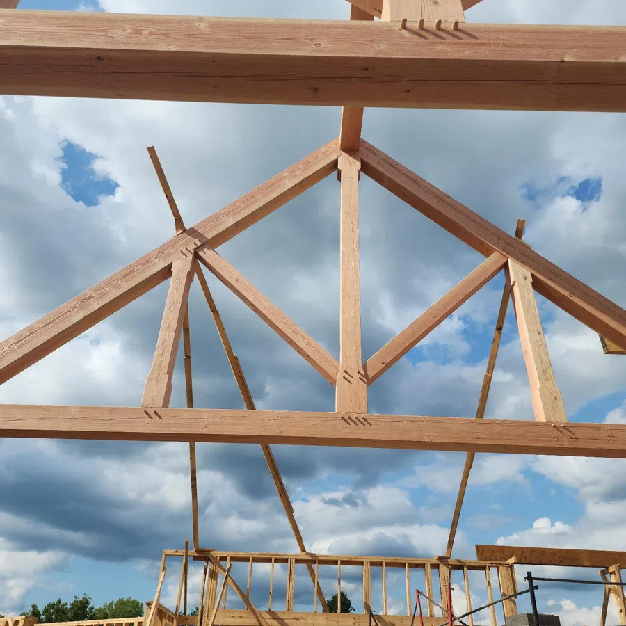Wooden roof trusses under construction against a partly cloudy blue sky background.