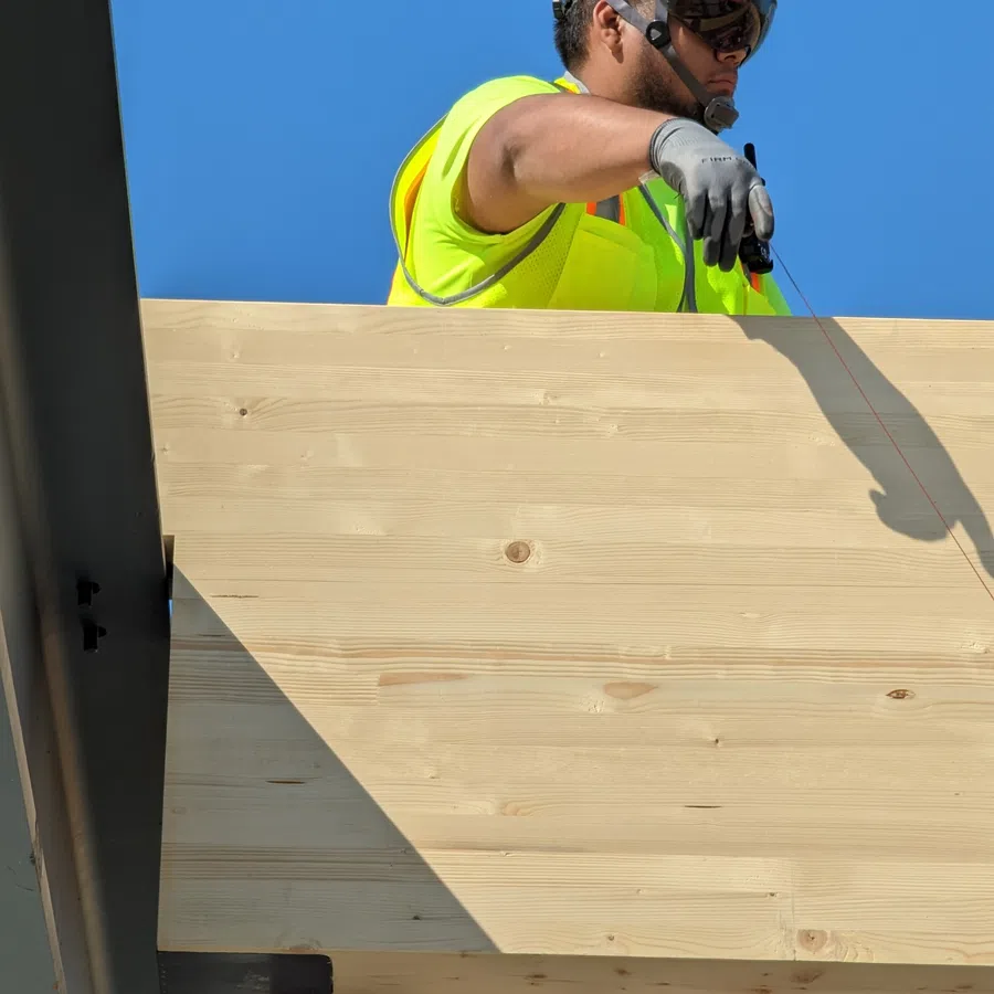 Construction worker wearing red helmet and neon safety vest operating elevated platform on a sunny day.