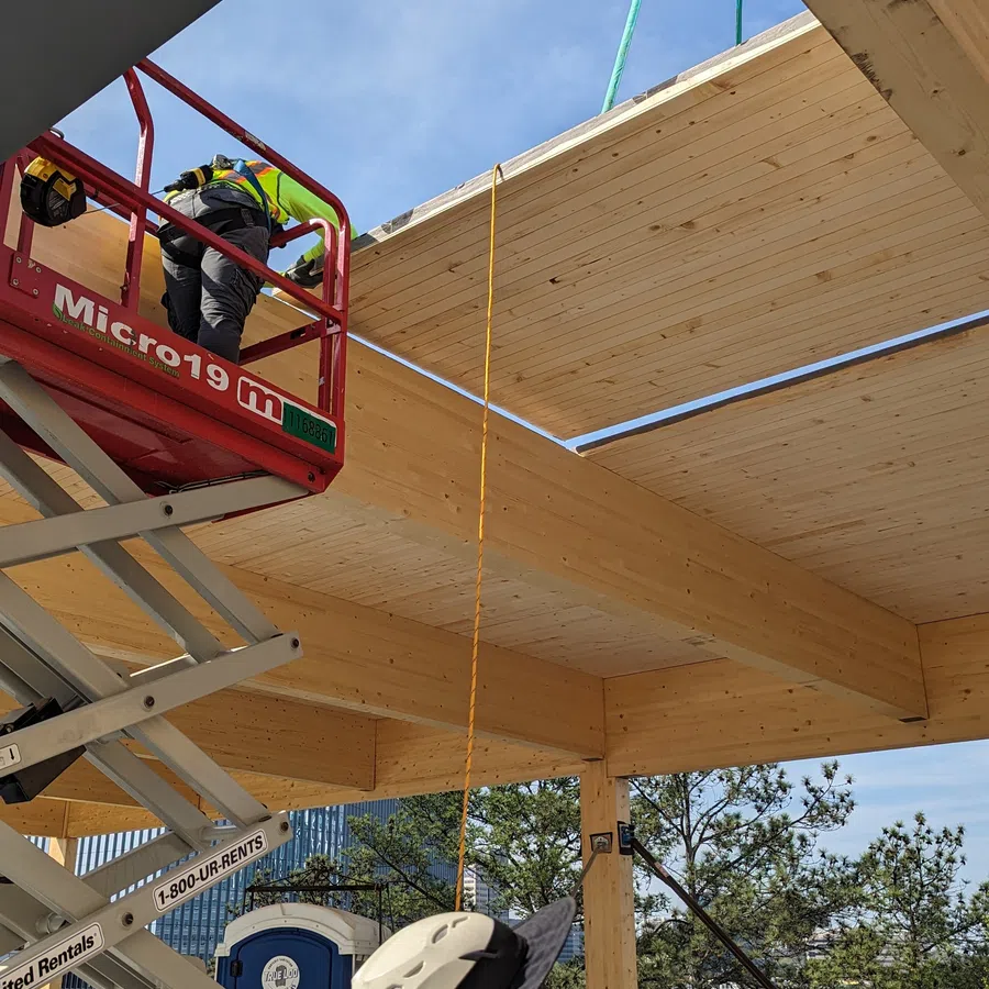 Construction workers installing large wooden panels using a scissor lift on a building site under clear blue sky