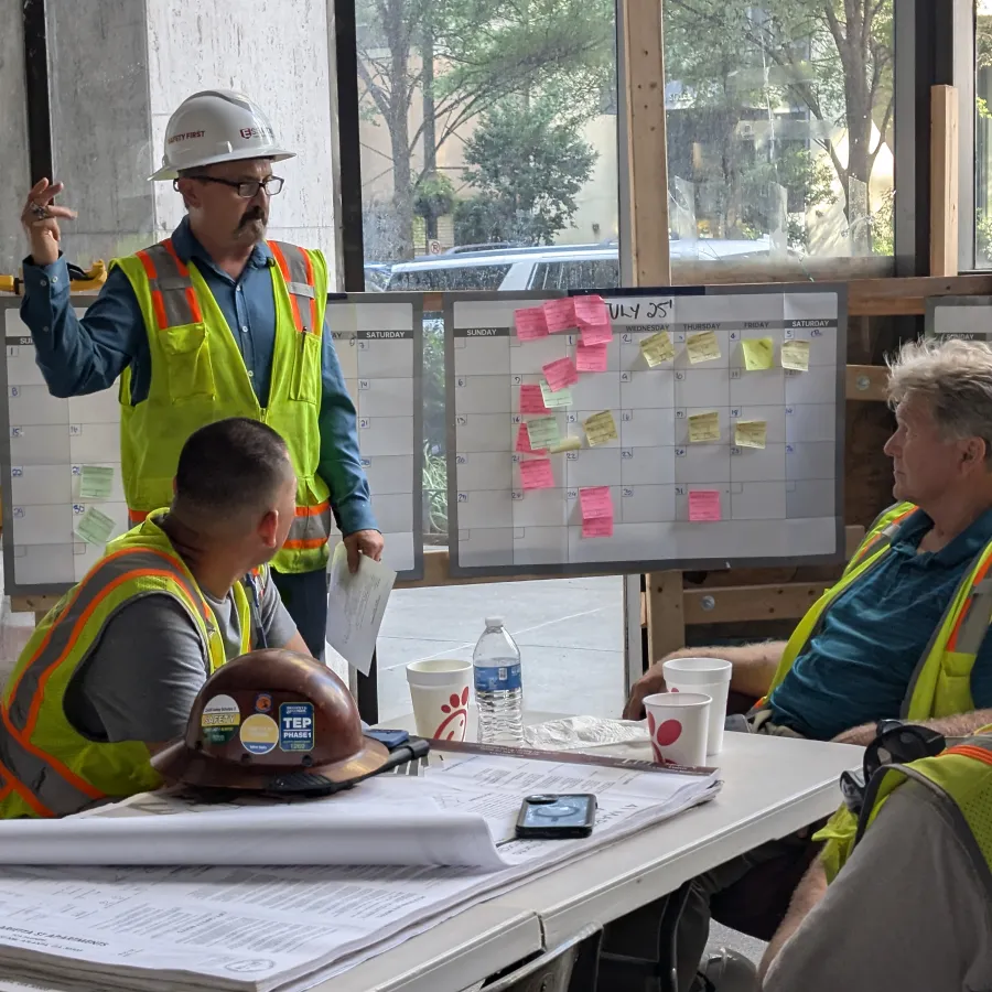 Construction team in safety vests and helmets discussing project plans and schedules in a meeting room.