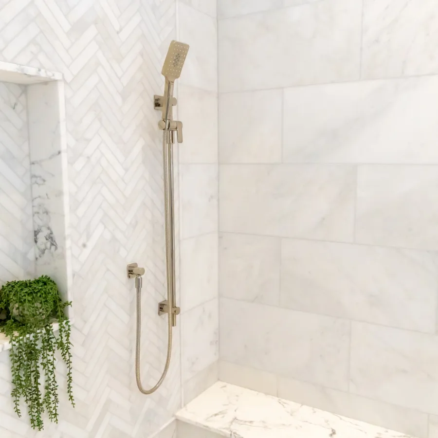 Modern shower design featuring marble tiles, a handheld showerhead, and green plants for a spa-like atmosphere.