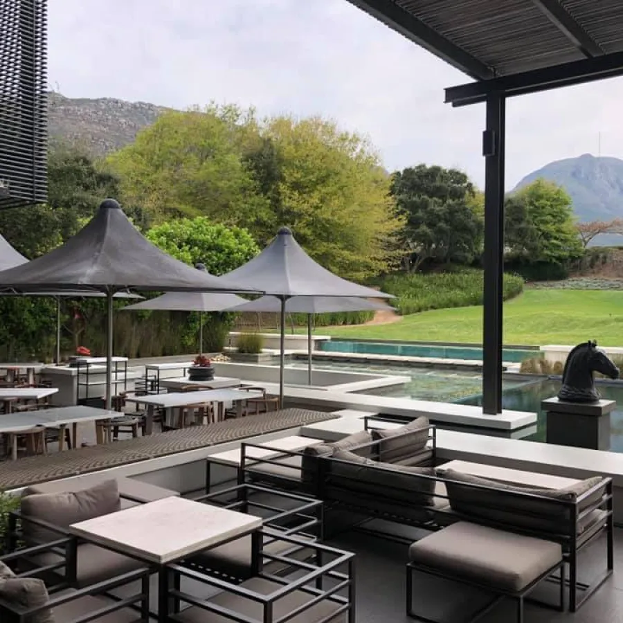 Outdoor patio with modern seating, umbrellas, pool, and mountain view under cloudy sky.