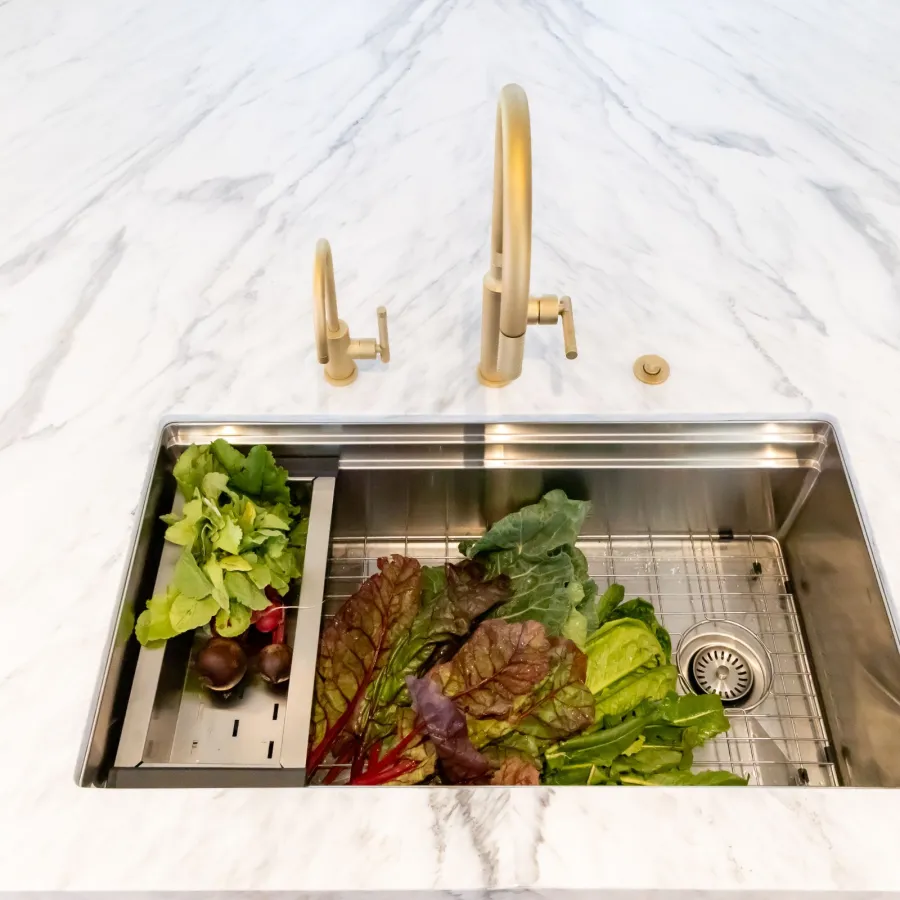 Modern kitchen sink with gold fixtures and fresh vegetables on a marble countertop.
