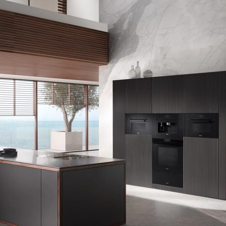 Modern black kitchen featuring sleek cabinets, marble walls, and ocean view windows.