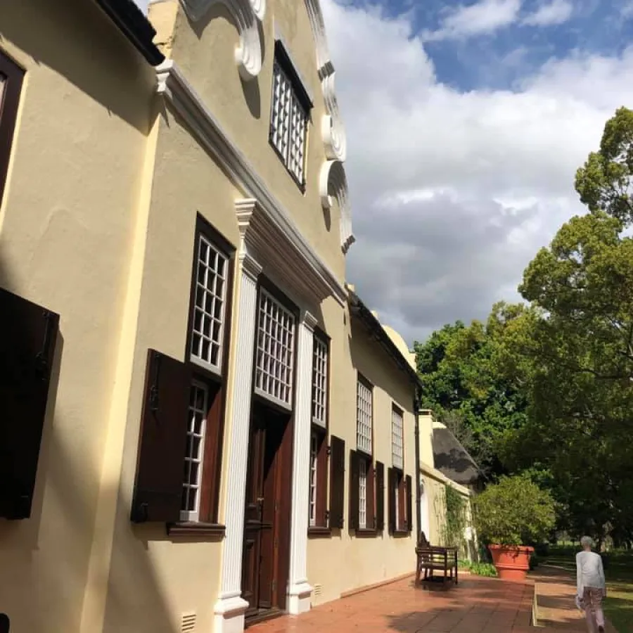 Historic Cape Dutch-style building with white decorative gables and shuttered windows under a blue sky.