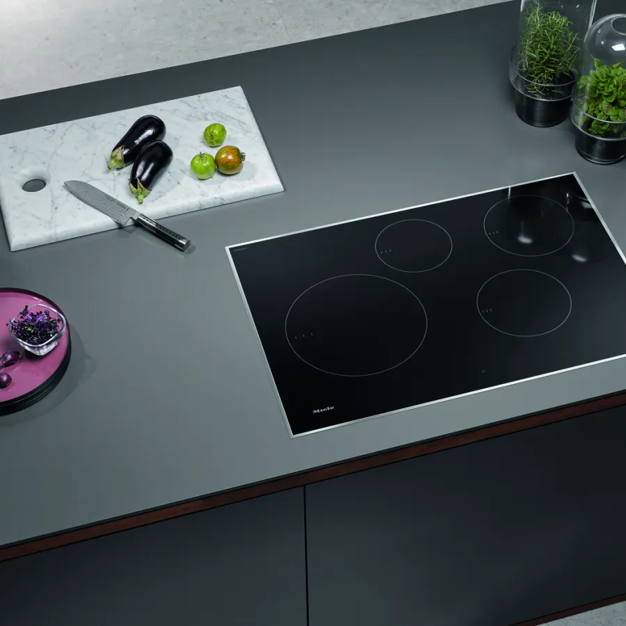Modern kitchen with a sleek induction cooktop, vegetables, and a marble cutting board for food prep.