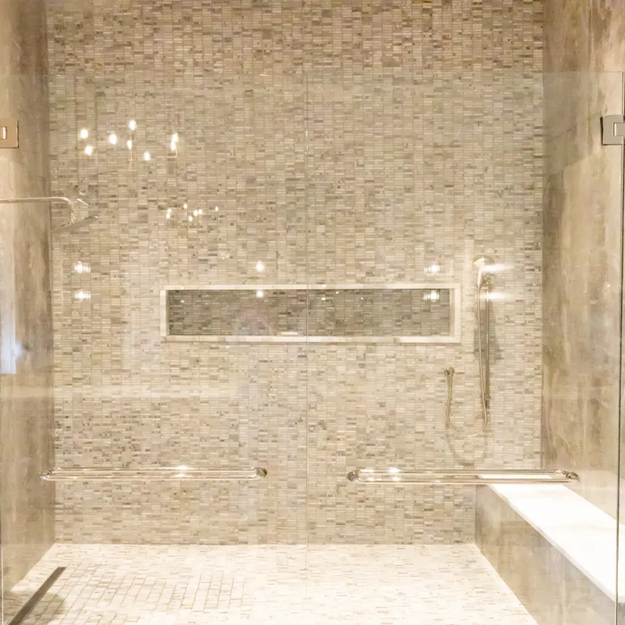 Luxurious modern shower with marble tiles and glass doors, featuring stylish lighting.