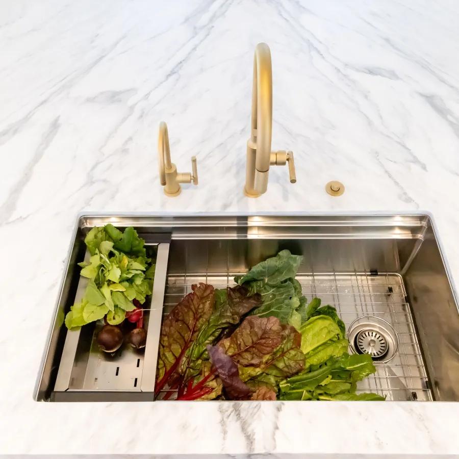 Stylish kitchen sink with fresh greens on a marble countertop and elegant gold fixtures.