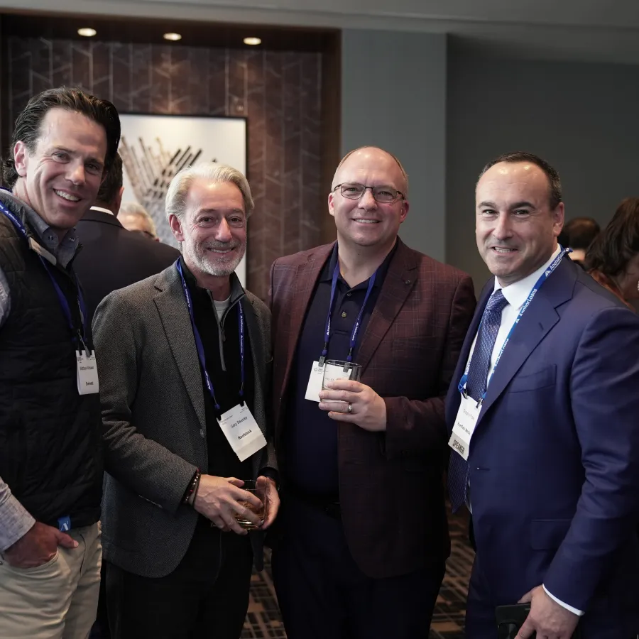 Four men in business attire smiling and posing together at a professional networking event indoors.