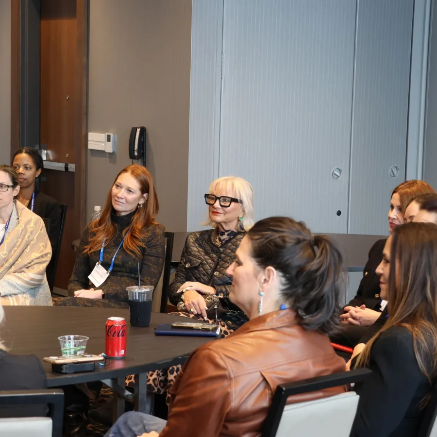 Diverse group of women seated around a conference table engaged in a meeting or discussion in a modern office room.