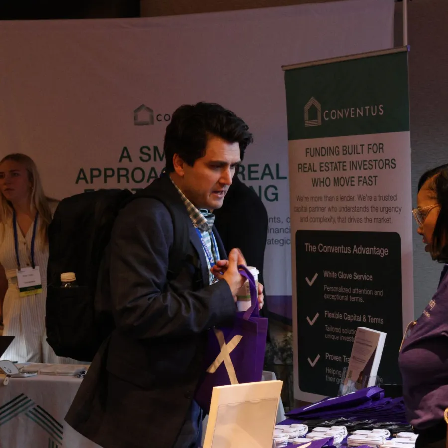 Business professionals interacting at a real estate investment funding booth with informational banners and promotional materials.