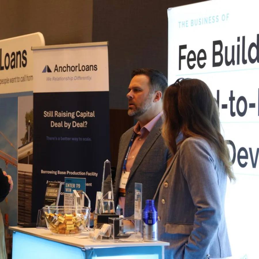 Three professionals engaged in conversation at the Anchor Loans booth during a business conference or trade show event.