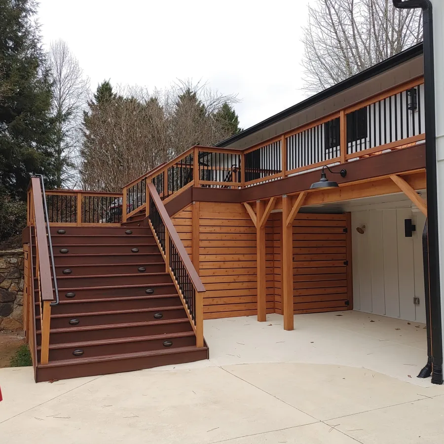 Modern wooden deck with stairs leading to upper level and red closed patio umbrella on concrete patio.