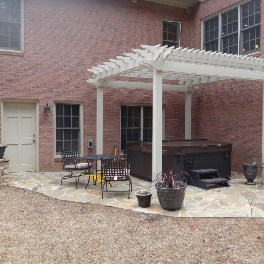 Backyard patio with pergola, hot tub, metal table and chairs, stone floor, and potted plants beside a brick house.