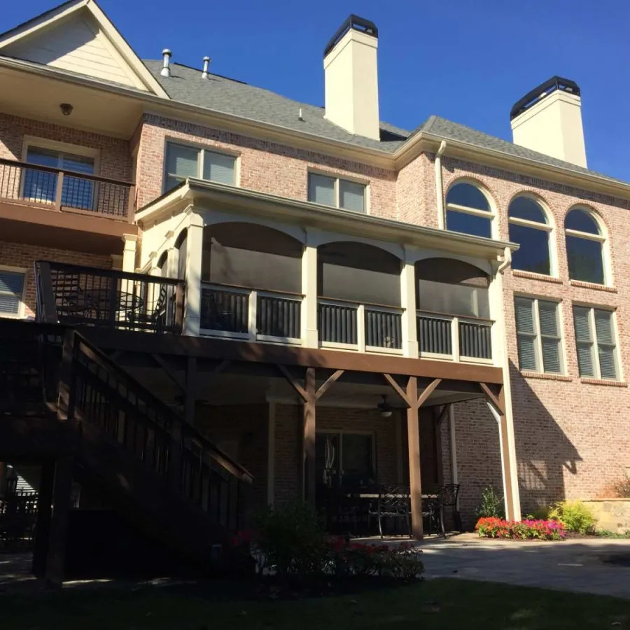 Large brick house with two chimneys, arched windows, covered balcony, and outdoor staircase under blue sky