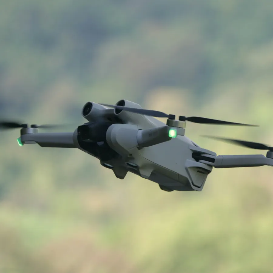 Close-up of a modern drone with spinning propellers flying outdoors against a blurred natural background
