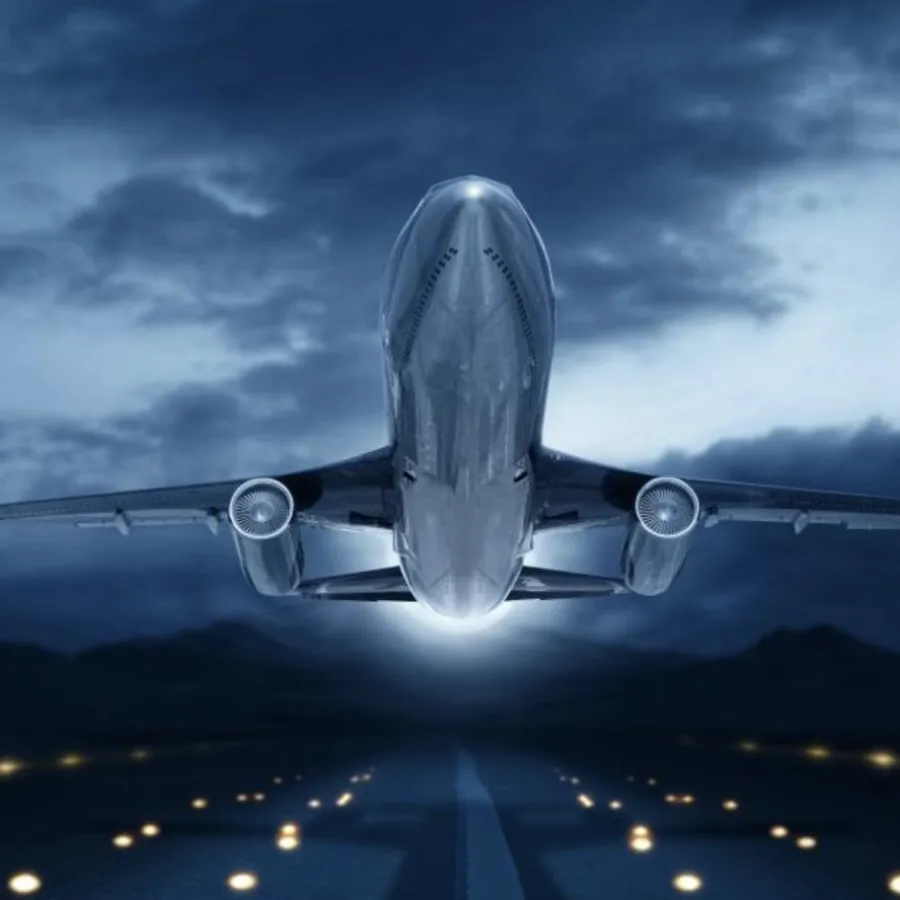 Aircraft taking off at night against a dramatic sky, illuminated runway lights in foreground.