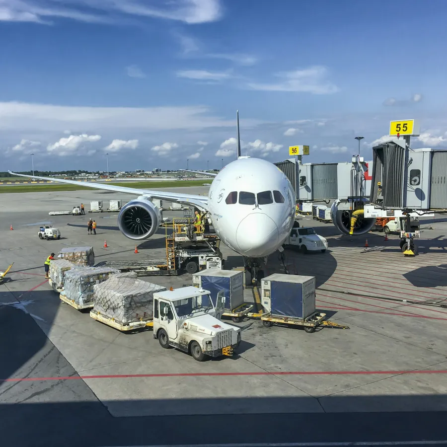 Large white airplane parked at airport gate 55 with cargo being loaded on a bright sunny day.