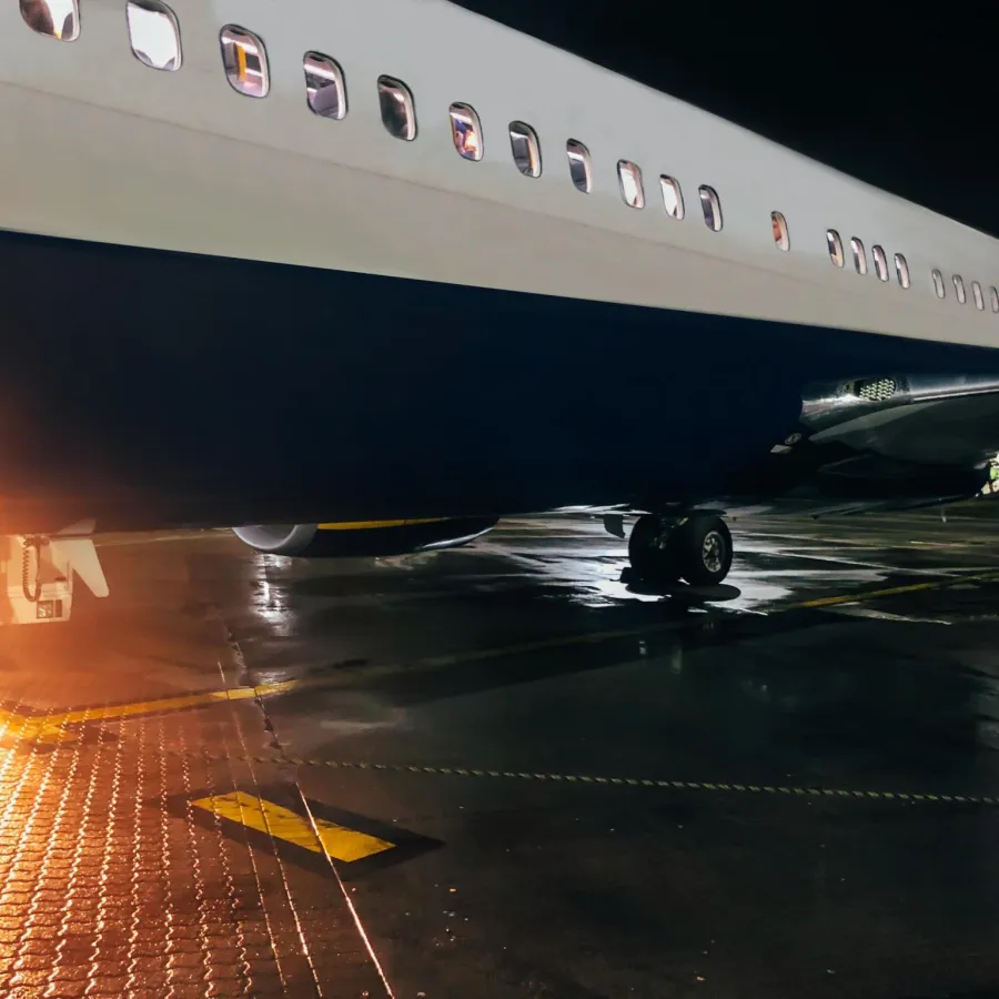 Close-up of airplane fuselage and engine on wet tarmac at night with glowing light reflections on surface