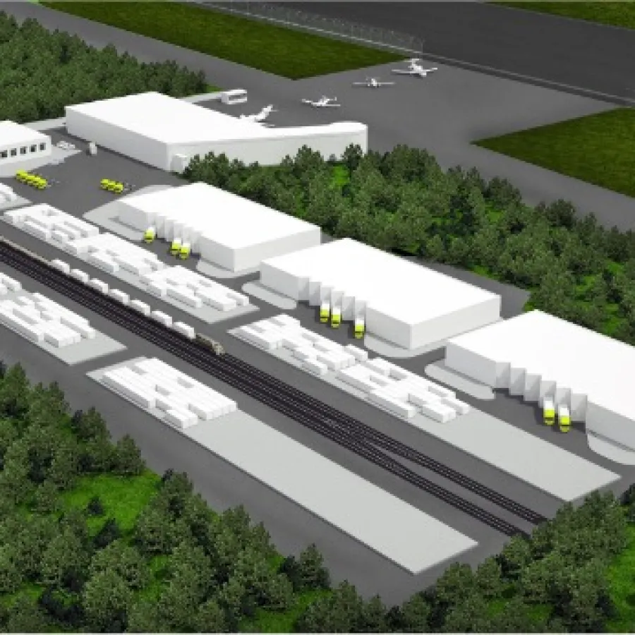 Aerial view of an industrial complex with warehouses, rail tracks, and airplanes near a runway surrounded by forest.