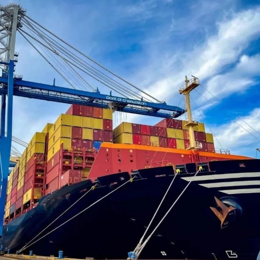Large cargo ship loaded with colorful containers docked at port under blue sky with cranes in background