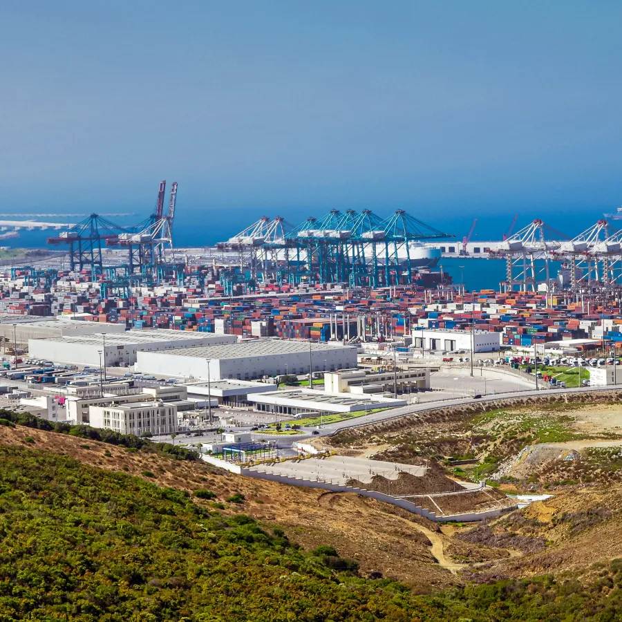 Aerial view of a busy shipping port with numerous containers, cranes, and industrial buildings by the sea.