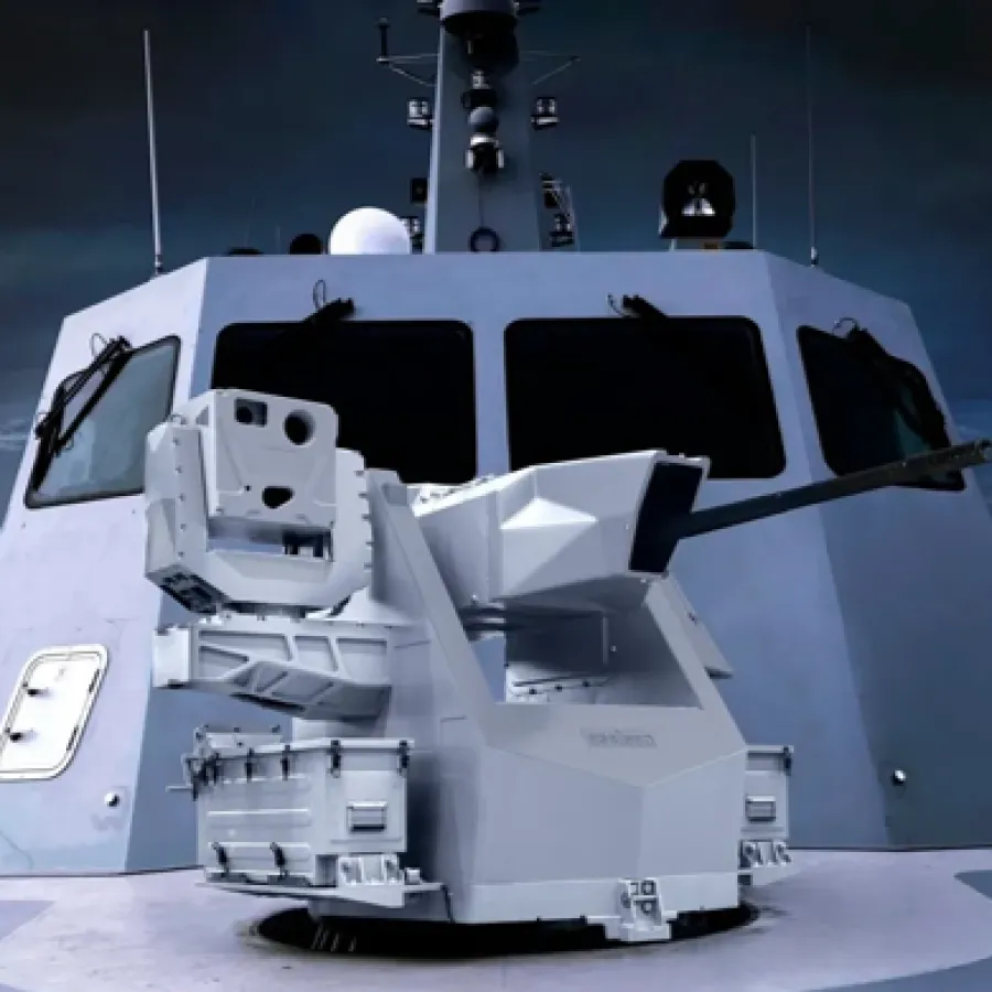 Modern naval gun turret mounted on a warship deck with stormy ocean background at dusk.