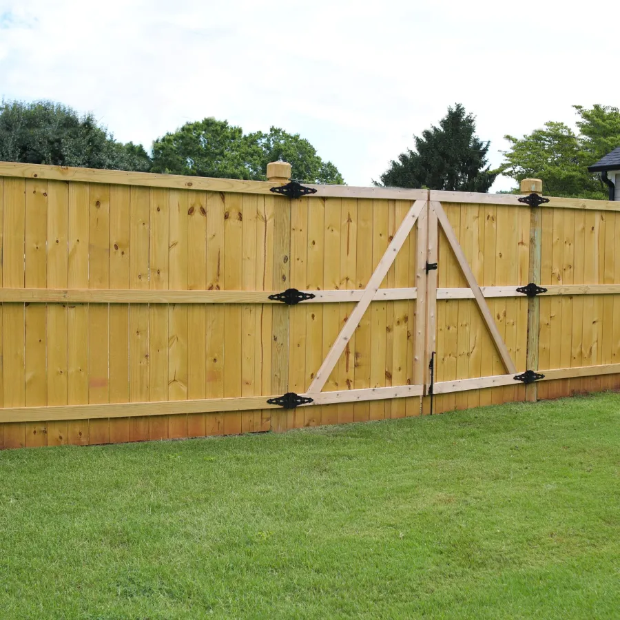 Newly installed wooden privacy fence with a double gate surrounding a backyard with green grass.