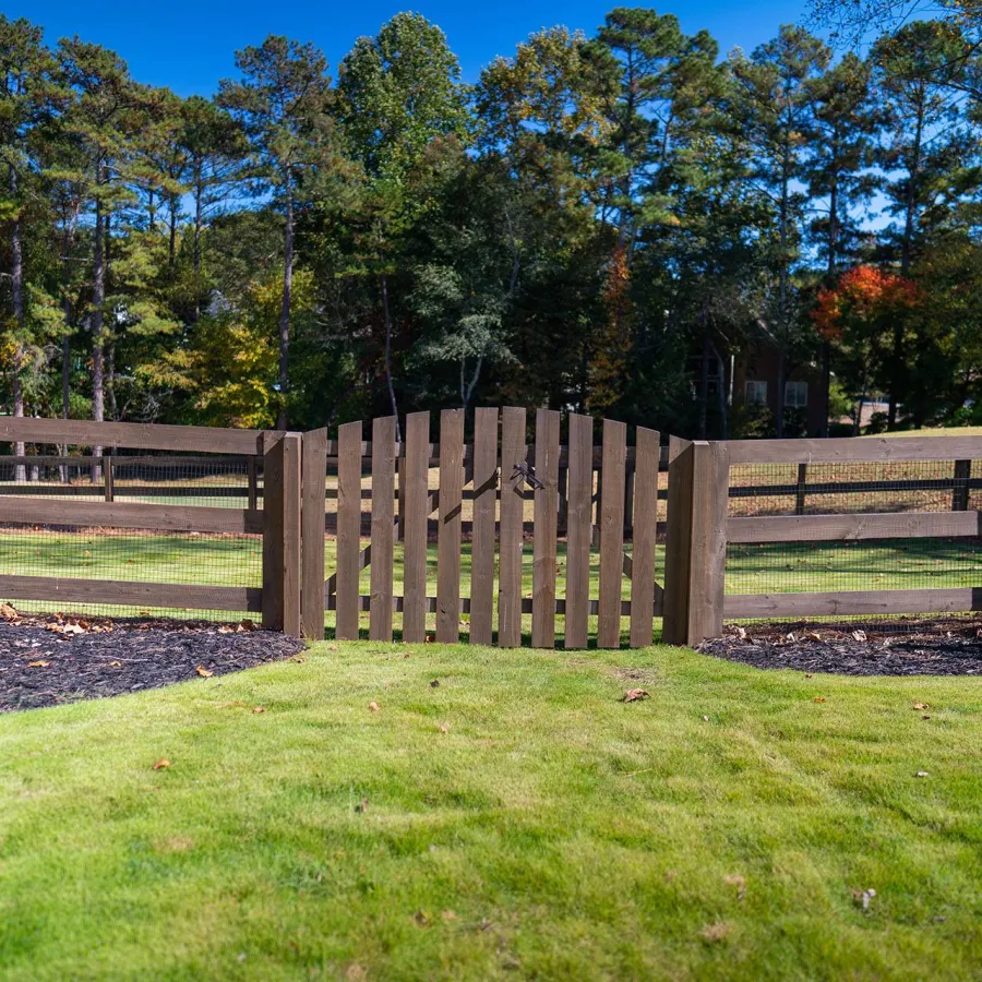 a fenced in yard with a wood gate and trees in the background