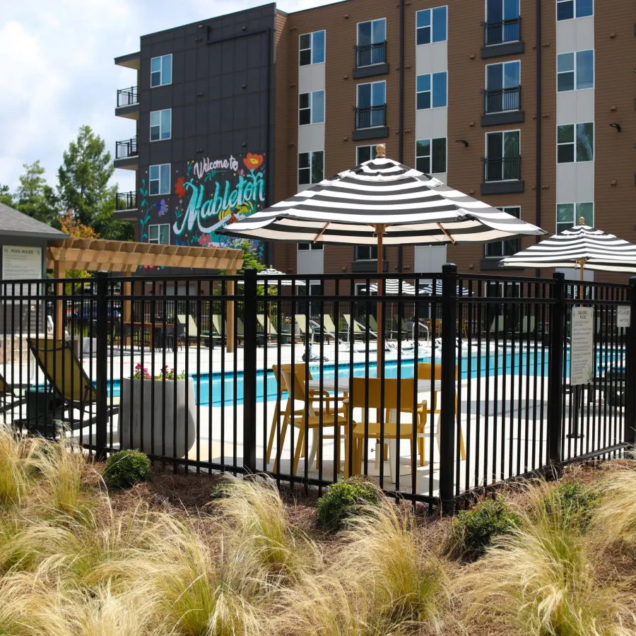 Modern apartment pool area with striped umbrellas, lounge chairs, and a colorful Welcome to Mableton mural.