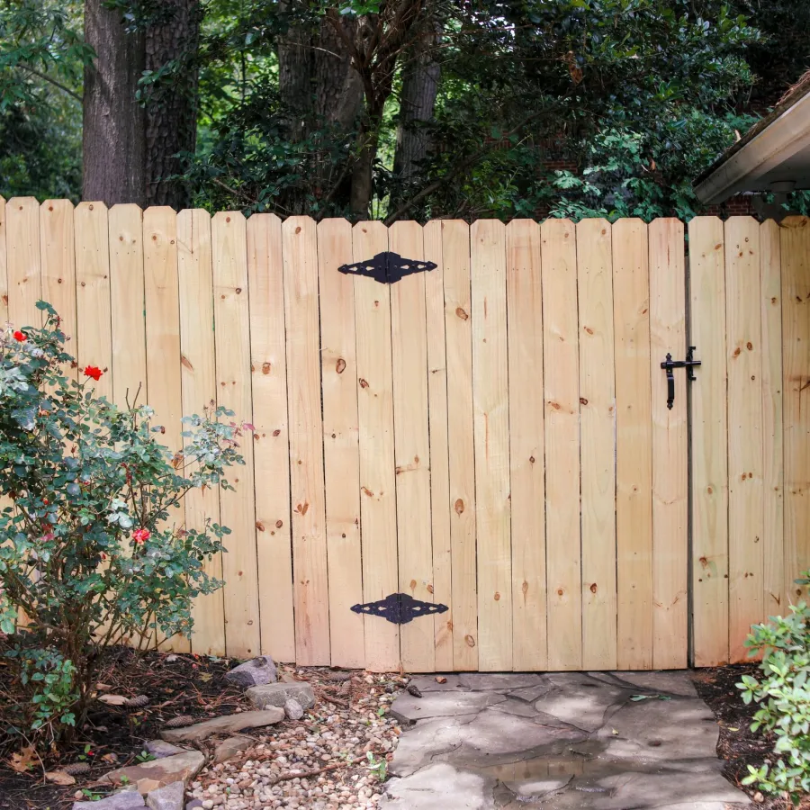 Wooden fence gate with black metal hinges next to house and rose bushes in garden
