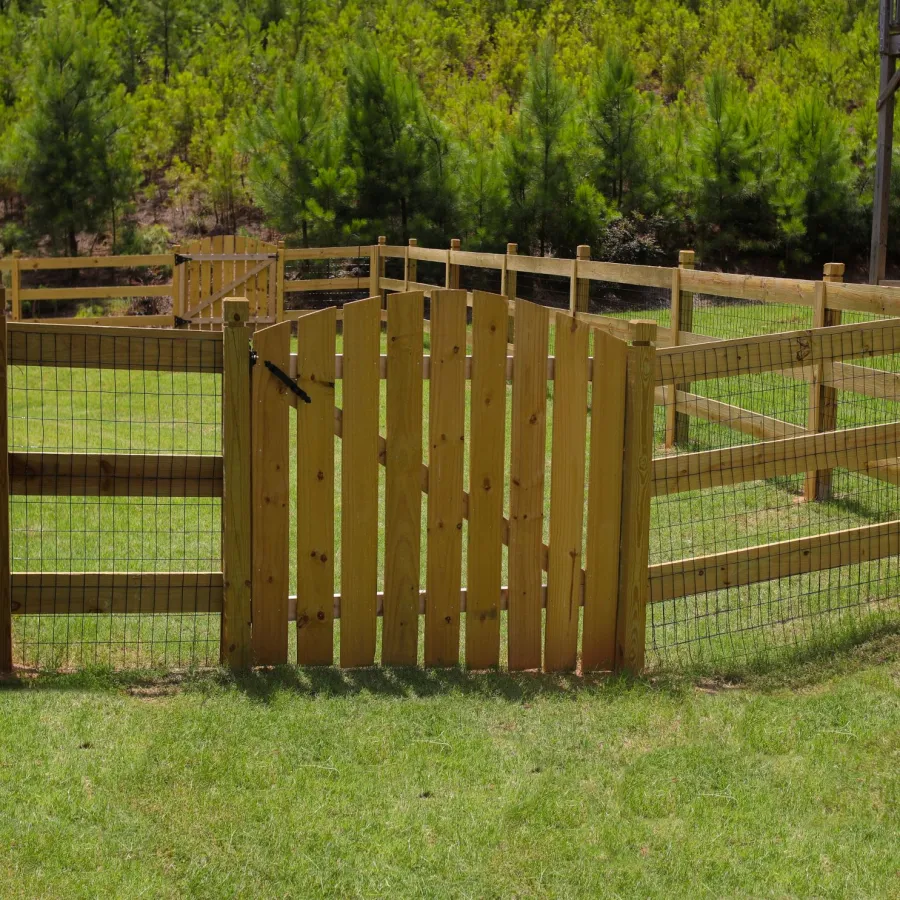 Wooden fence with wire mesh surrounding a grassy backyard area next to a house and trees.