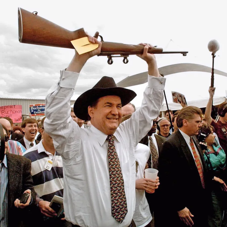Pat Buchanan in a suit and tie holding a gun