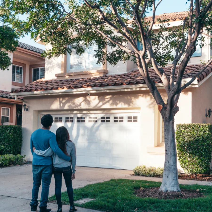Couple admiring a beautiful suburban home with lush greenery and a welcoming exterior.