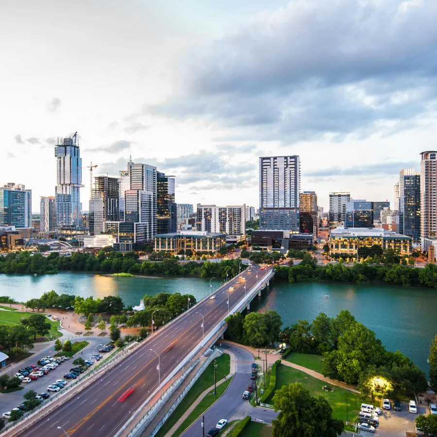 Panoramic view of Austin skyline with bridges and river under a cloudy sky during golden hour.