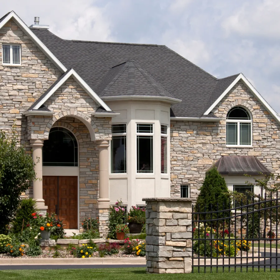 Elegant stone house with a landscaped garden and decorative gate under a bright sky.