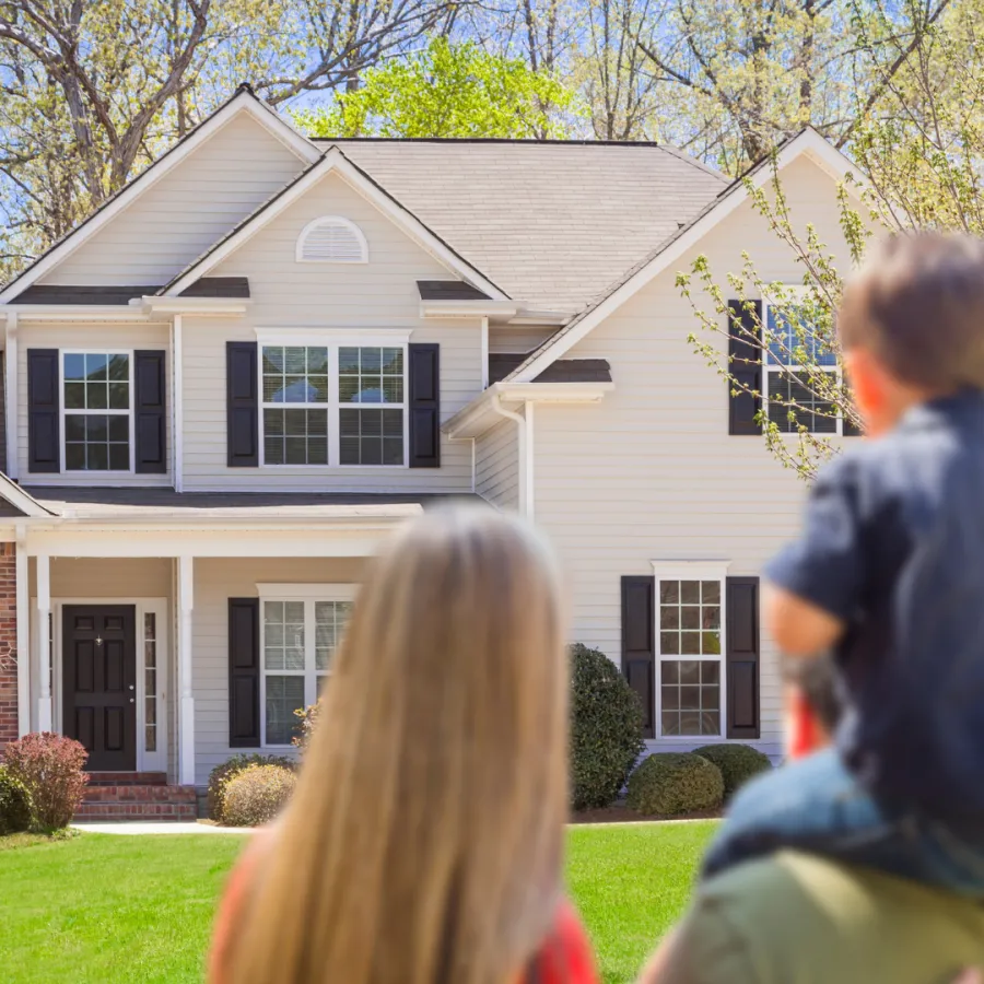 Family enjoying a sunny day in front of a beautiful suburban home with lush greenery.