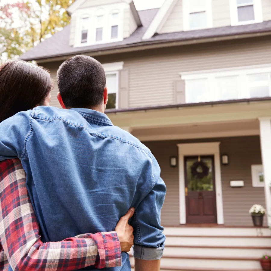 Couple admiring their new home with a welcoming porch and lush greenery in front.